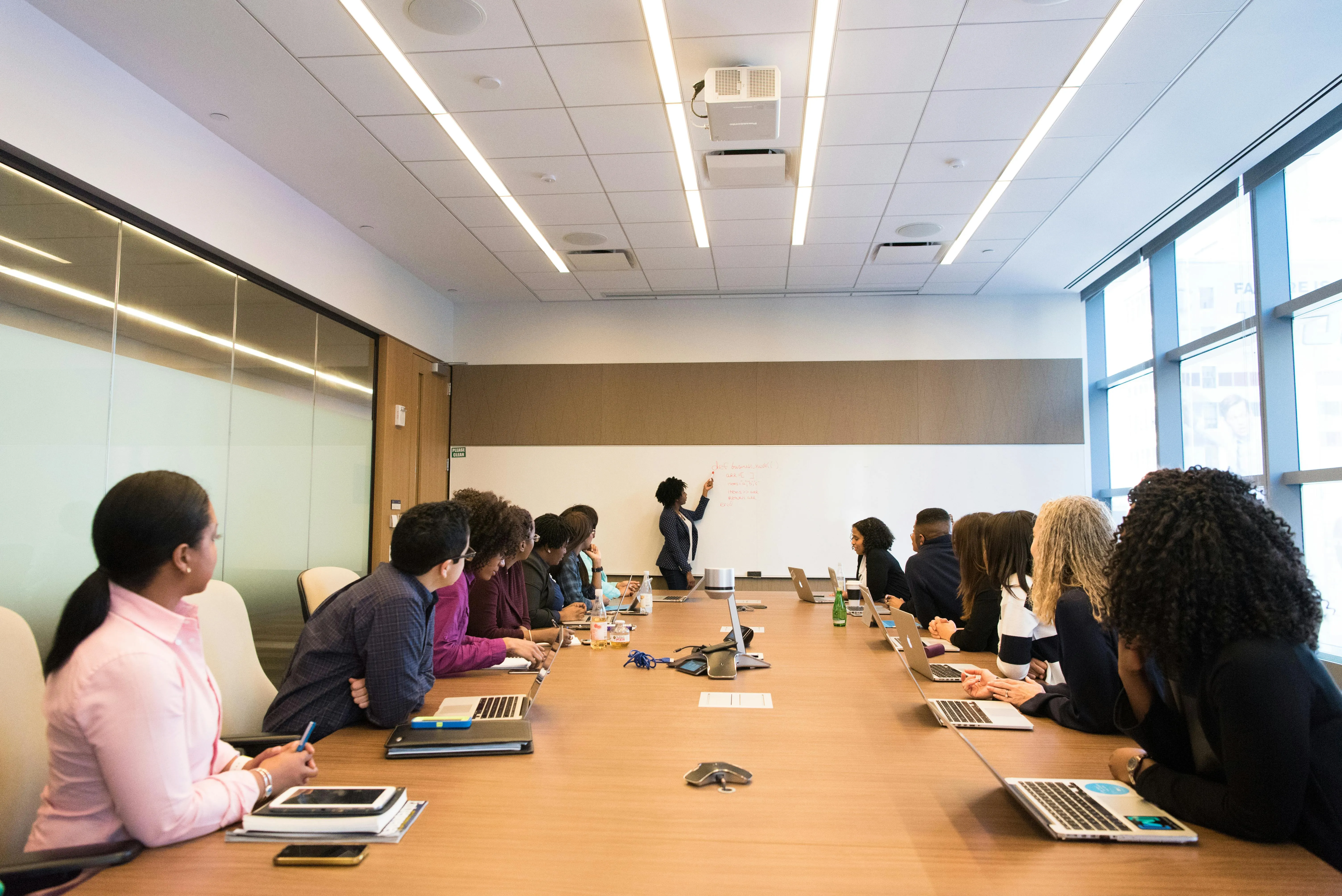 A business office board room meeting with lots of people sitting around like a Board Meeting.