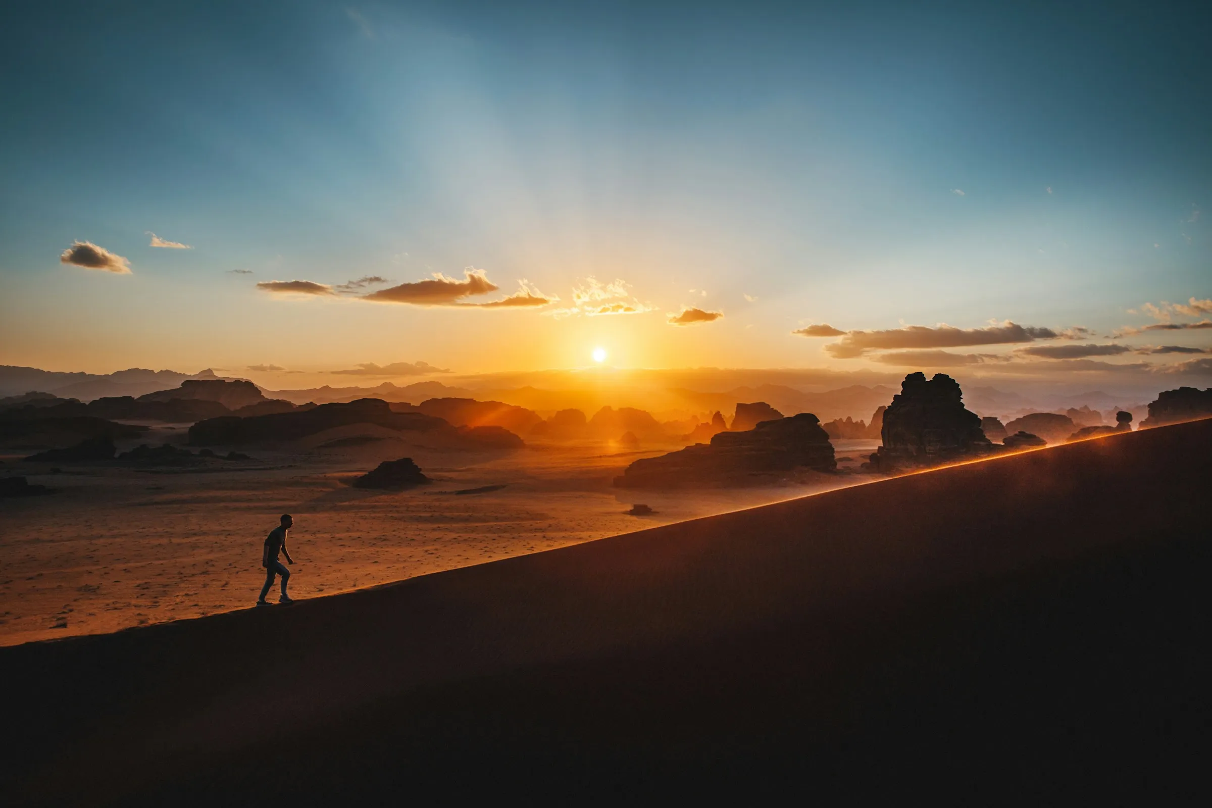 A beautiful sunset over a Desert, with the silouette of a man walking from left to right up a slight inclined hill.
