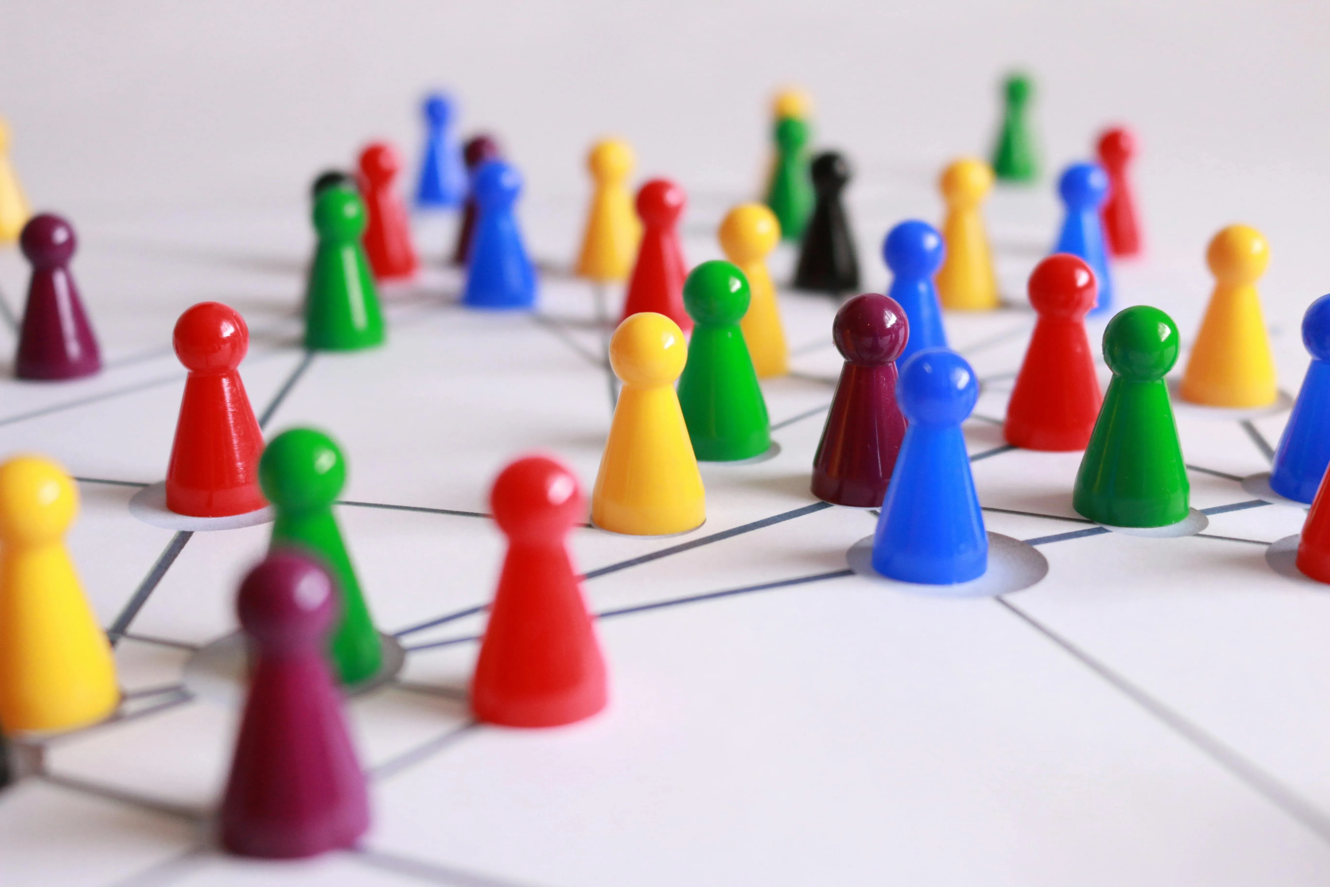 Colourful pins that look a bit like people from a board game. They are arranged haphazerdly on a piece of paper with lots of lines drawn on that intersect, showing a network of people.