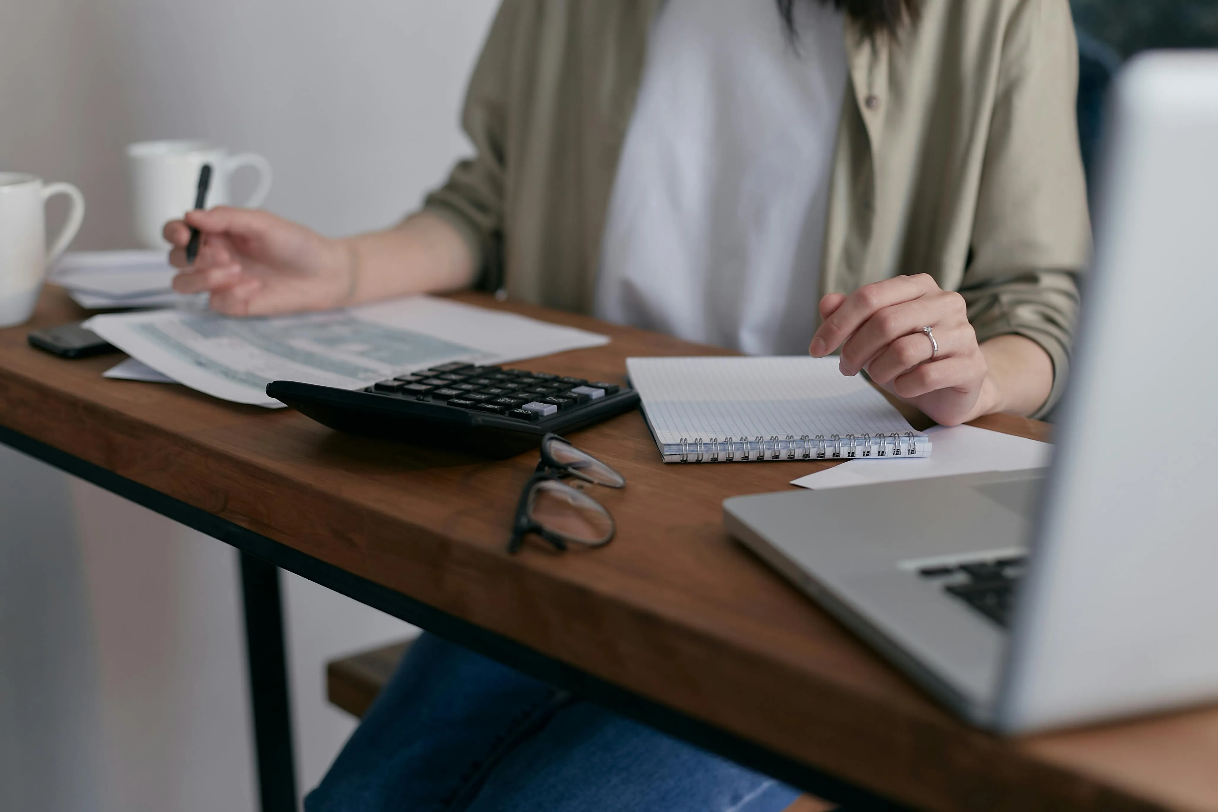 A woman sitting at a table filling out a tax return, with a calculator nearby, glasses and a laptop..