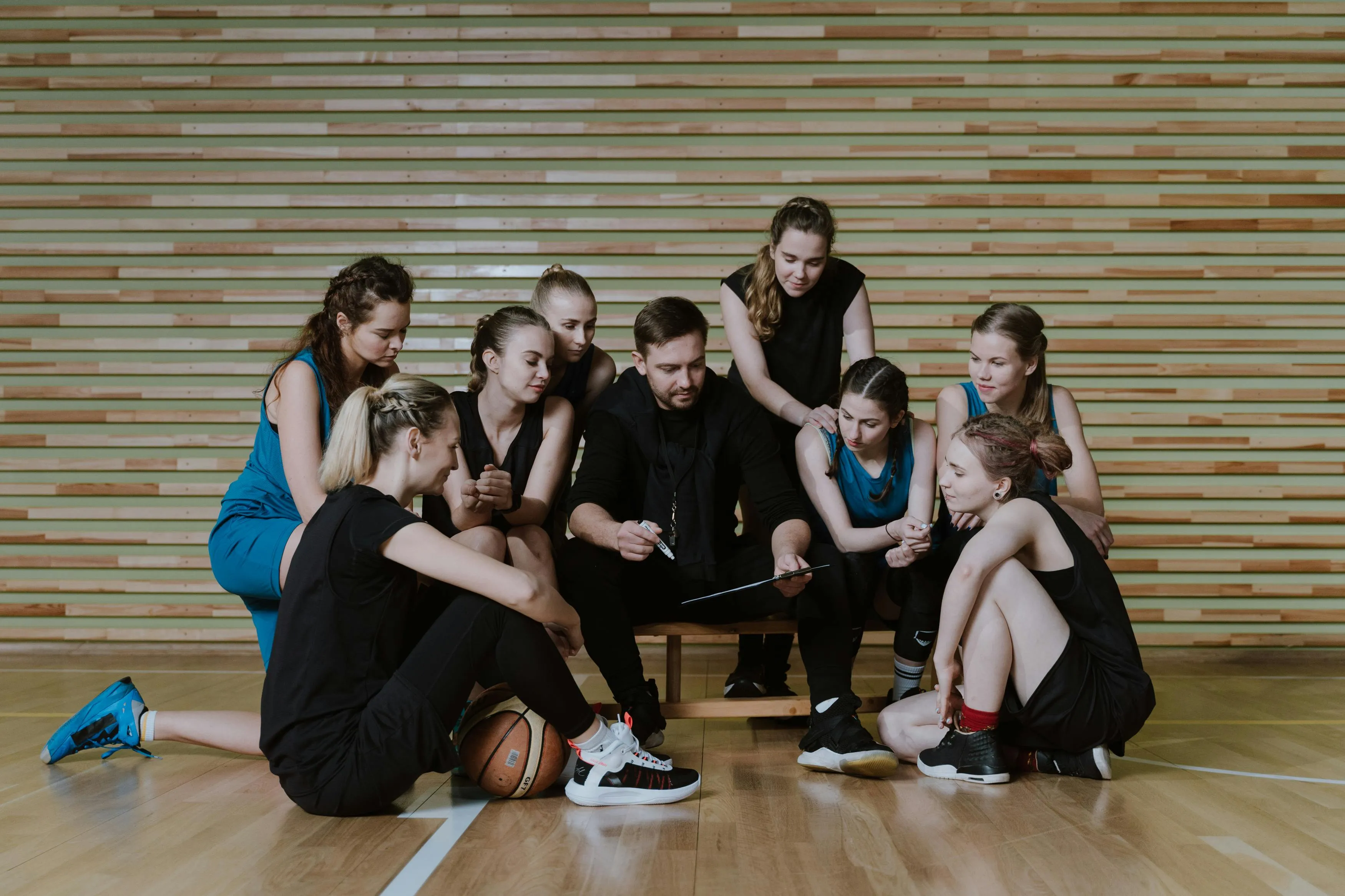 A women's basketball team sitting around their coach, who has a marker and board in his hand showing the plan.